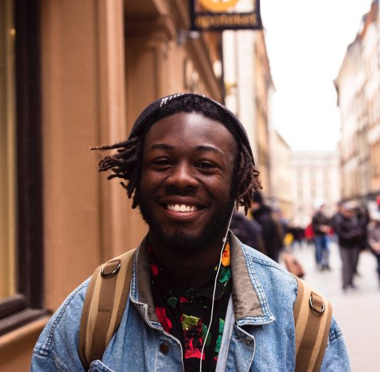 Jeune homme souriant dans une rue passante.