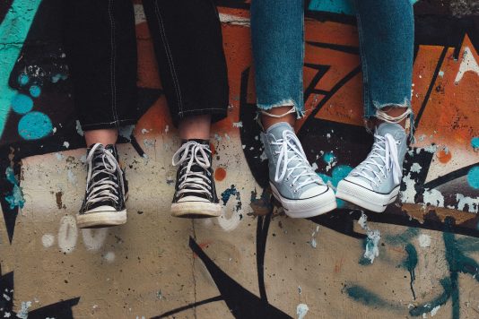 Deux paires de jambes avec des souliers devant un mur avec des grafitis.
