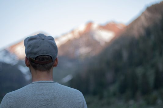 Jeune homme de dos devant une montagne.