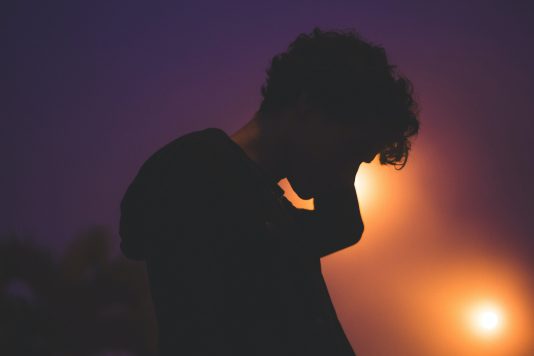 Silhouette d'un jeune homme sur un fond violet et illuminé.
